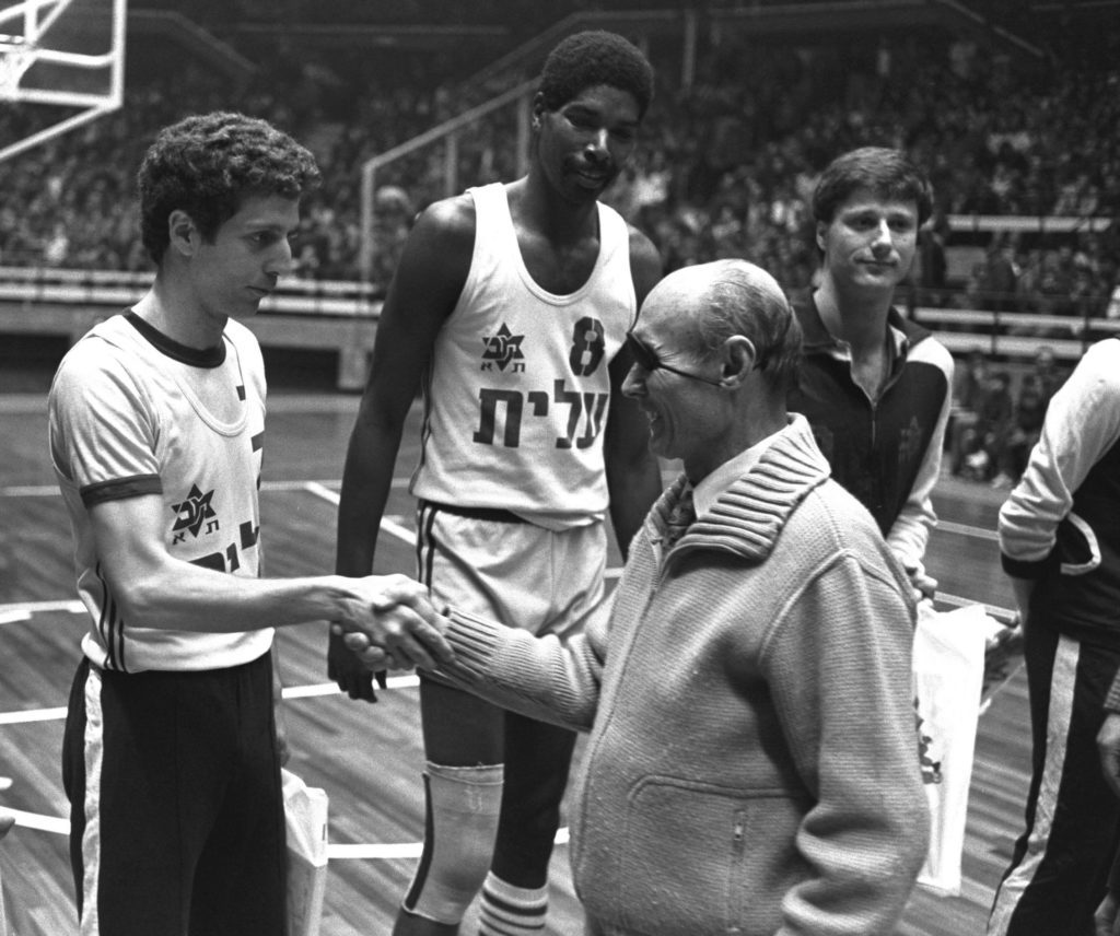 MK MOSHE DAYAN SHAKING HANDS WITH MACABBI TEL AVIV BASKETBALL PLAYER MOTTI AROESTI, AS AULCI PERRY & MIKY BERKOVITZ LOOK ON